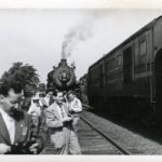 Numerous people standing in front of a train on the tracks