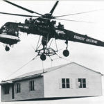 Black and white photograph of a helicopter in flight, hauling a house